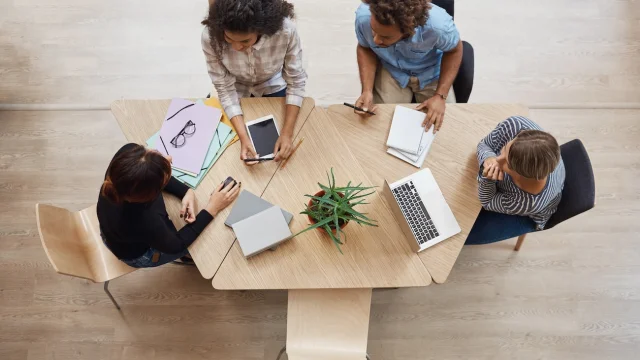 Vista dall'alto di un gruppo di giovani imprenditori professionisti seduti a un tavolo in uno spazio di coworking, mentre discutono i profitti dell'ultimo progetto di squadra, utilizzando laptop, tablet digitale e smartphone